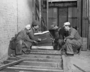 Construction workers crouch surface which has had floorboards remo Old Photo