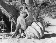 Grass skirted Joan Collins poses against a palm tree for film 'Gir- Old Photo