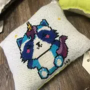 Hand stitched cross stitched pillow of a blue Unicoon( Unicorn-Raccoon)