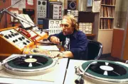 Howard Hesseman talks into a microphone in a broadcast booth in a - Old Photo