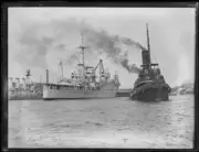 Tugboat travelling away from the docked aircraft carrier H.M.A.S. - Old Photo