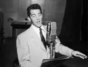 singer Dean Martin stands behind a microphone looking at a music s- Old Photo