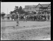 Golfer T. Howard hitting a ball in front of crowd by a club house,- Old Photo